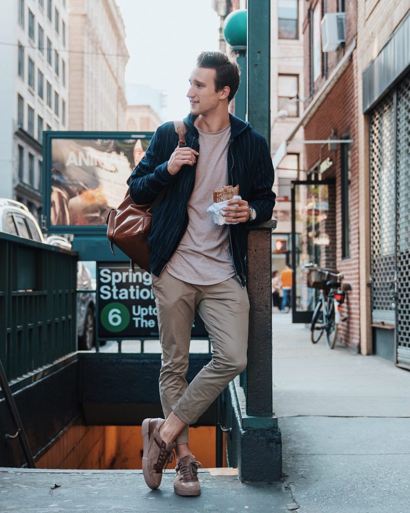 picture of a men standing beside subway stairs holding a sandwich and a brown bag in the other hand 