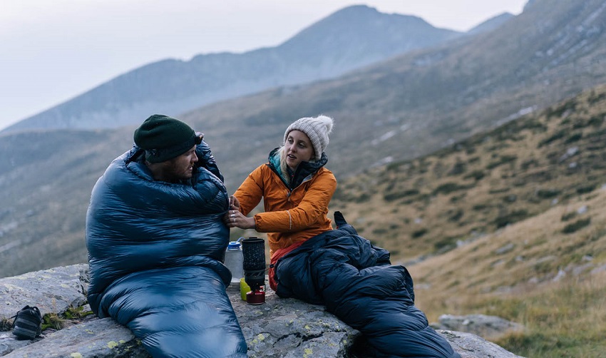 Close-up of a couple in sleeping bags seating on a rock