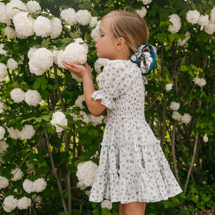 little girl in white dress smelling flowers
