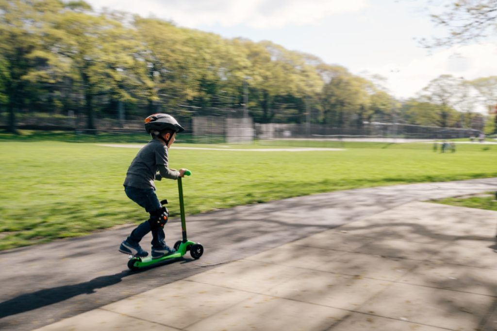 a little boy in knee pads rides a scooter
